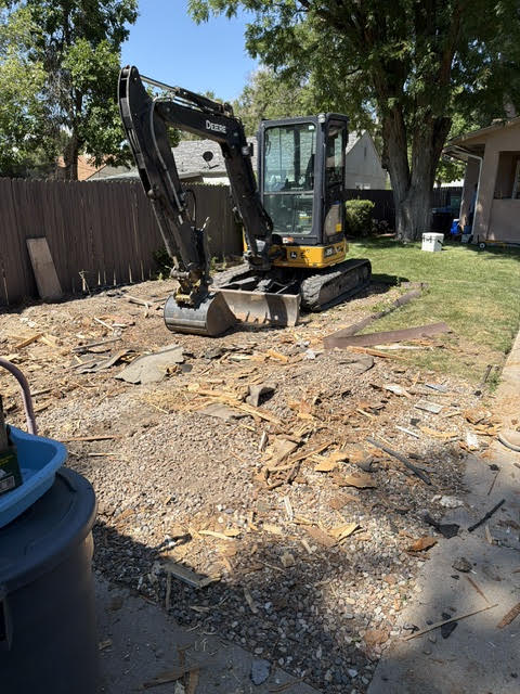 Excavator clearing demolition debris from a backyard in Pueblo, Colorado